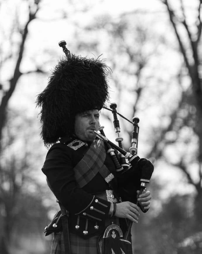Medium close up shot of playing bagpipes, in full Highland Dress
