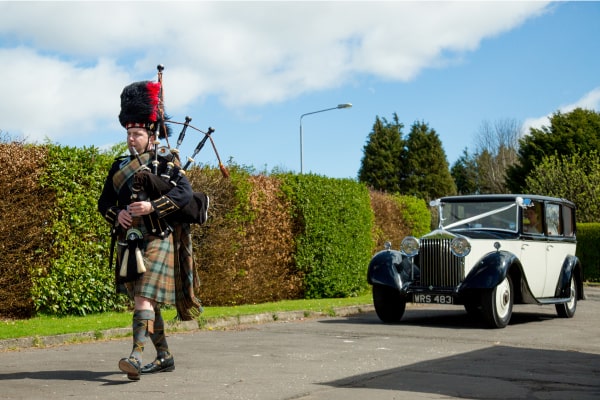 Piping in full Highland Dress while leading a wedding car