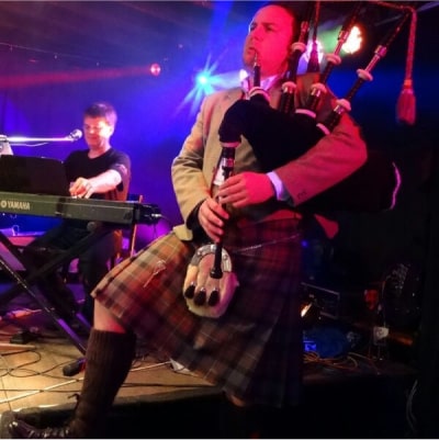 Playing bagpipes in front of stage at an informal party setting